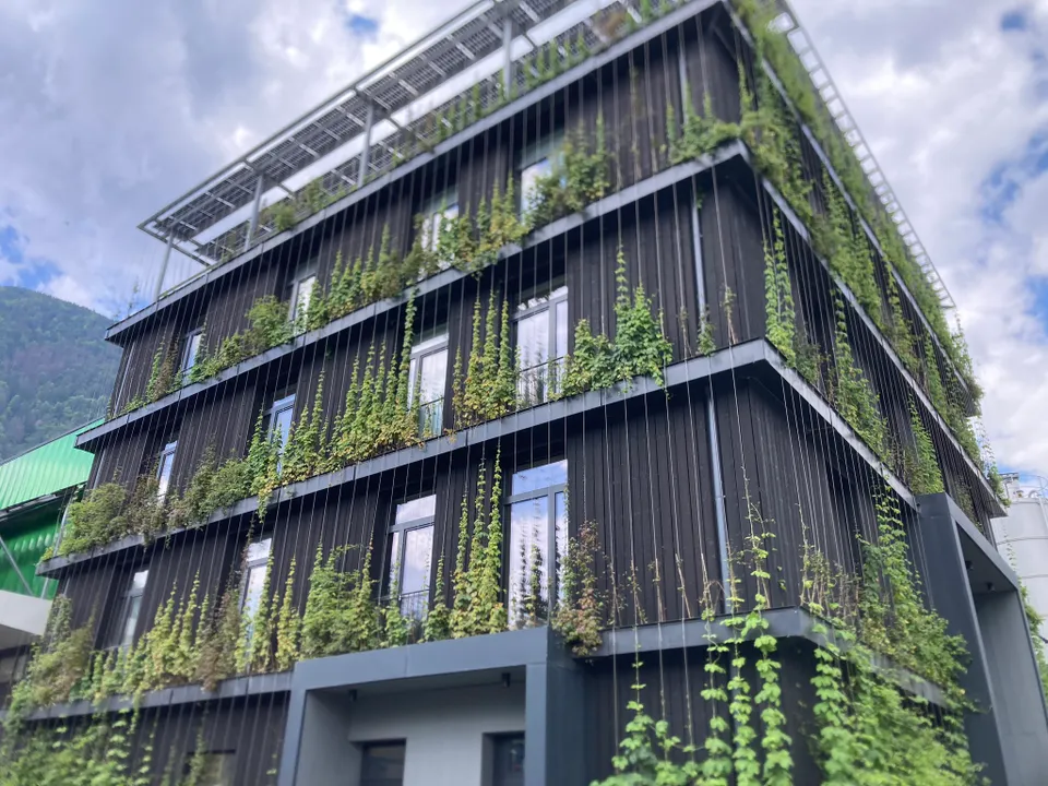 Modernes mehrstöckiges Gebäude mit Holzfassade und üppiger vertikaler Begrünung an den Außenwänden. - LINEA FUTURA GREENING