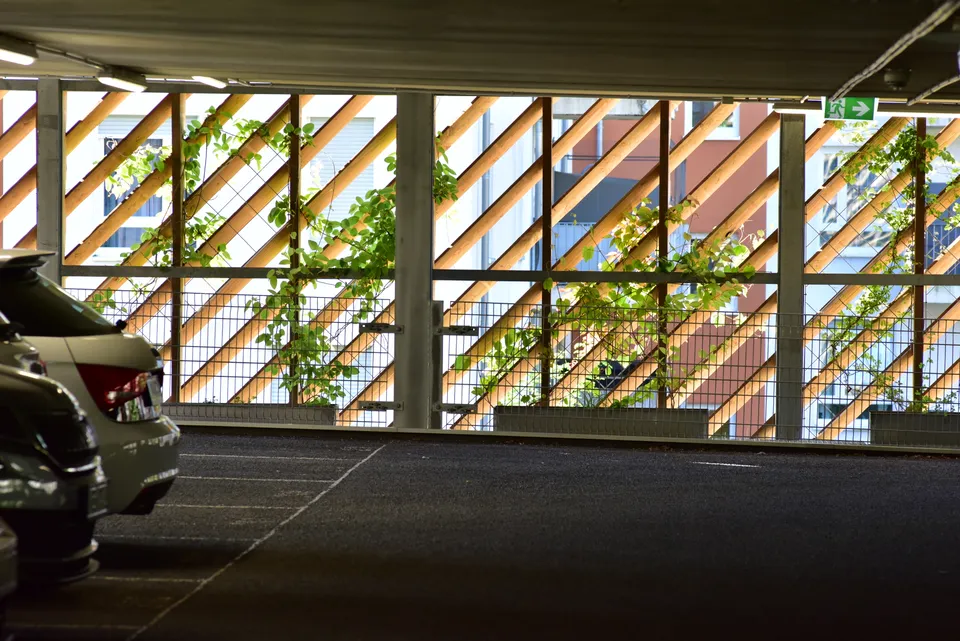 Blick in ein modernes Parkhaus mit geparkten Autos und einer begrünten Holz- und Gitterfassade. - LINEA FUTURA GREENING