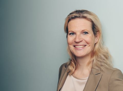 Lächelnde Frau mit blonden Haaren in beigefarbenem Mantel - Coaching Komplizin