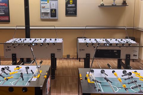 Ein Raum mit mehreren Tischfußballkästen, Pokalen und Werbeplakaten an den Wänden. - Happy Billard