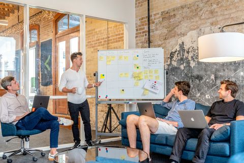 Büroraum mit Whiteboard, Sofas und Laptops, in dem eine Gruppe von Mitarbeitern zusammenarbeitet - Coaching Komplizin