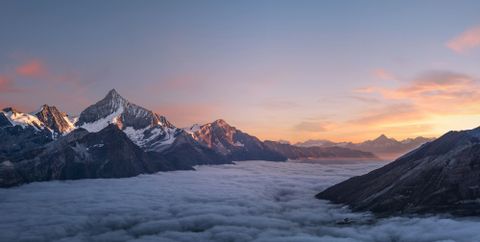 Majestätische Berglandschaft mit schneebedeckten Gipfeln, die sich über einem Nebelmeer erheben, bei Sonnenuntergang. - Mut Mach Lehre