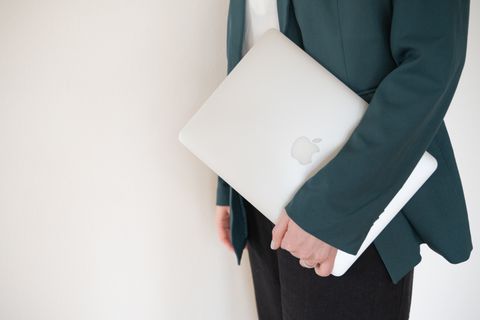 Auf diesem Bild sieht man nur einen Teil des Oberkörpers von Sanja. Sie trägt einen dunkelgrünen Blazer und hat ein Apple Macbook in der Hand. Sanja.Studio | Brand Design