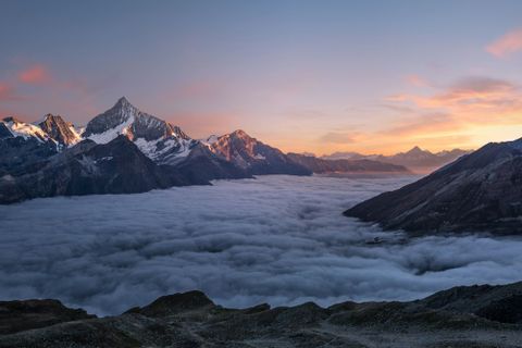 Majestätische Berglandschaft mit schneebedeckten Gipfeln, die sich über einem Nebelmeer erheben, bei Sonnenuntergang. - Mut Mach Lehre